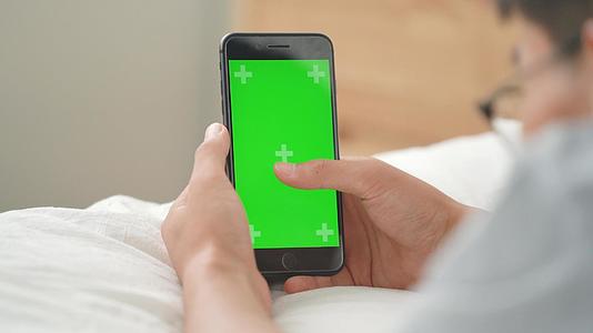 4k男生躺在床上玩绿幕手机视频的预览图