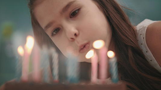 美丽的女孩在生日蛋糕上吹蜡烛火焰慢动作视频的预览图