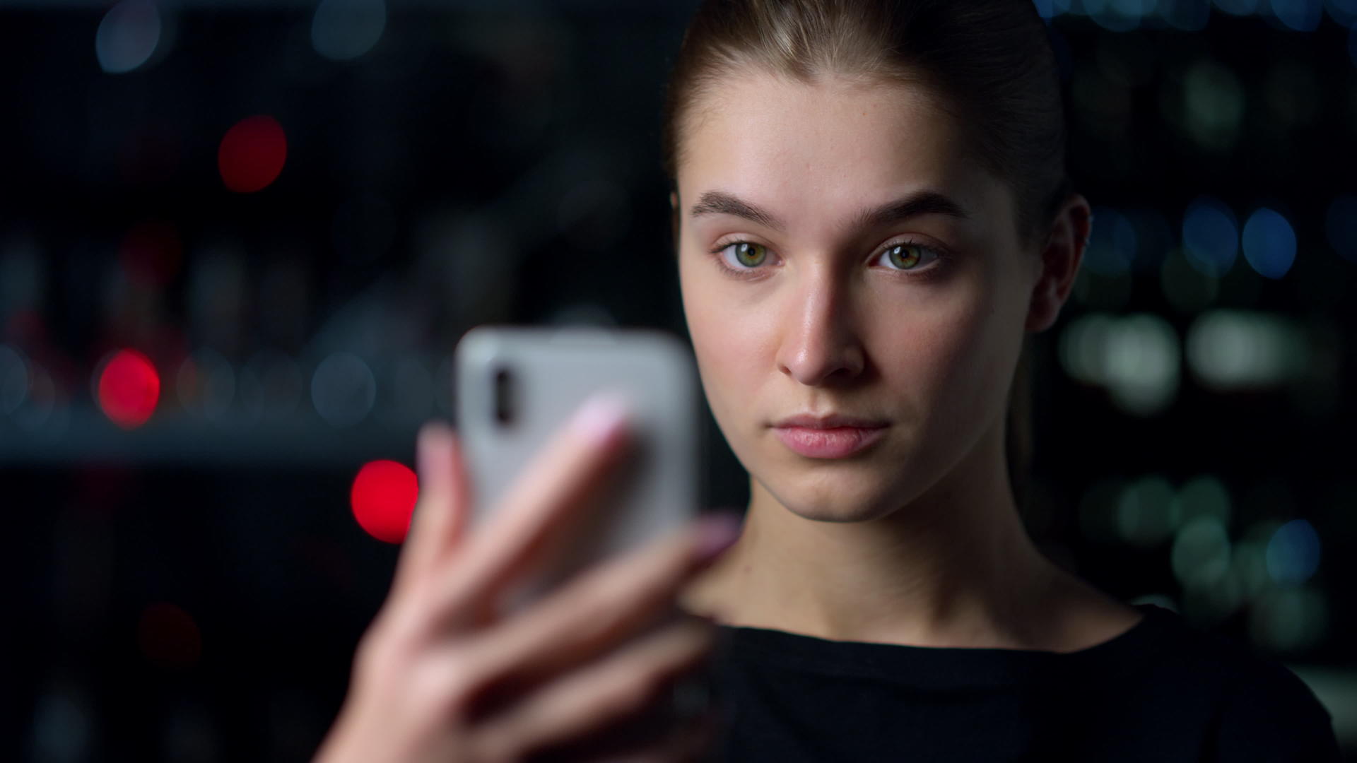 严肃的女孩用智能手机在夜间背景上自拍视频的预览图