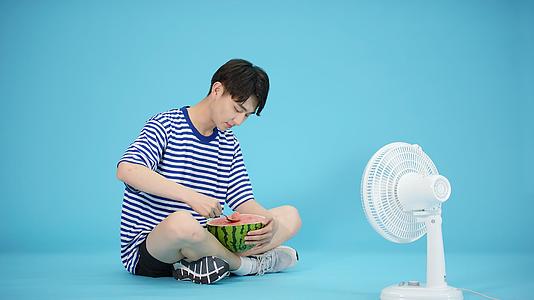 夏日吹风扇吃西瓜的男青年视频的预览图
