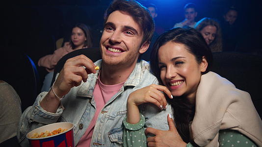 年轻情侣在电影院看电影开心地笑着视频的预览图