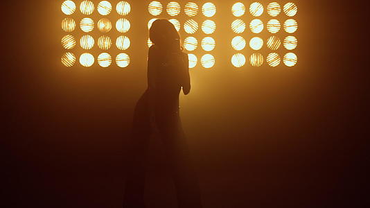 年轻女歌手在灯光下用复古麦克风跳舞唱歌视频的预览图