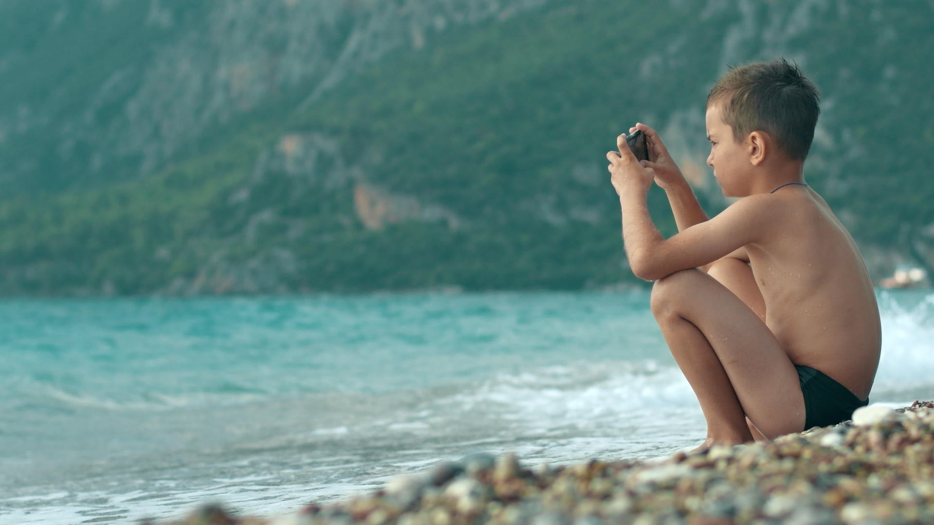 小男孩暑假在海边看手机视频的预览图