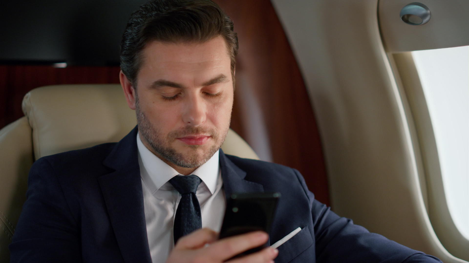 英俊的企业家在旅行飞机商务舱使用智能手机视频的预览图