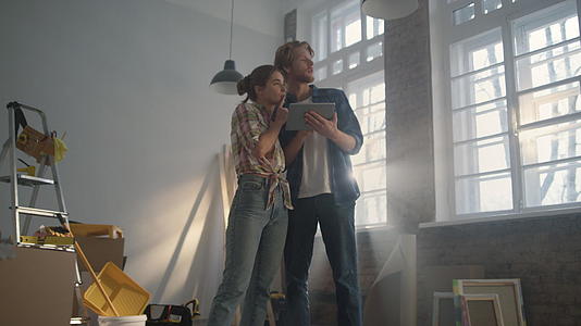 年轻夫妇的家在新房间里看平板电脑讨论家庭装修的想法视频的预览图