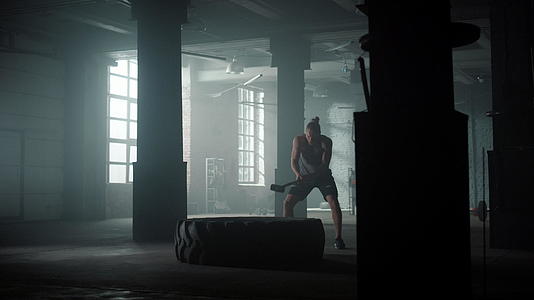 在体育俱乐部做力量锻炼的肌肉男用锤子打大轮胎视频的预览图