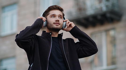 年轻男性在户外用耳机听歌舞视频的预览图