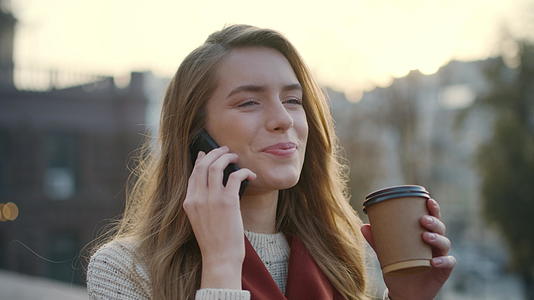 美女在户外喝咖啡时用手机打电话视频的预览图