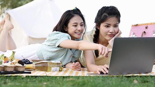 4k春游野餐户外野炊闺蜜趴在垫子上看电脑视频的预览图