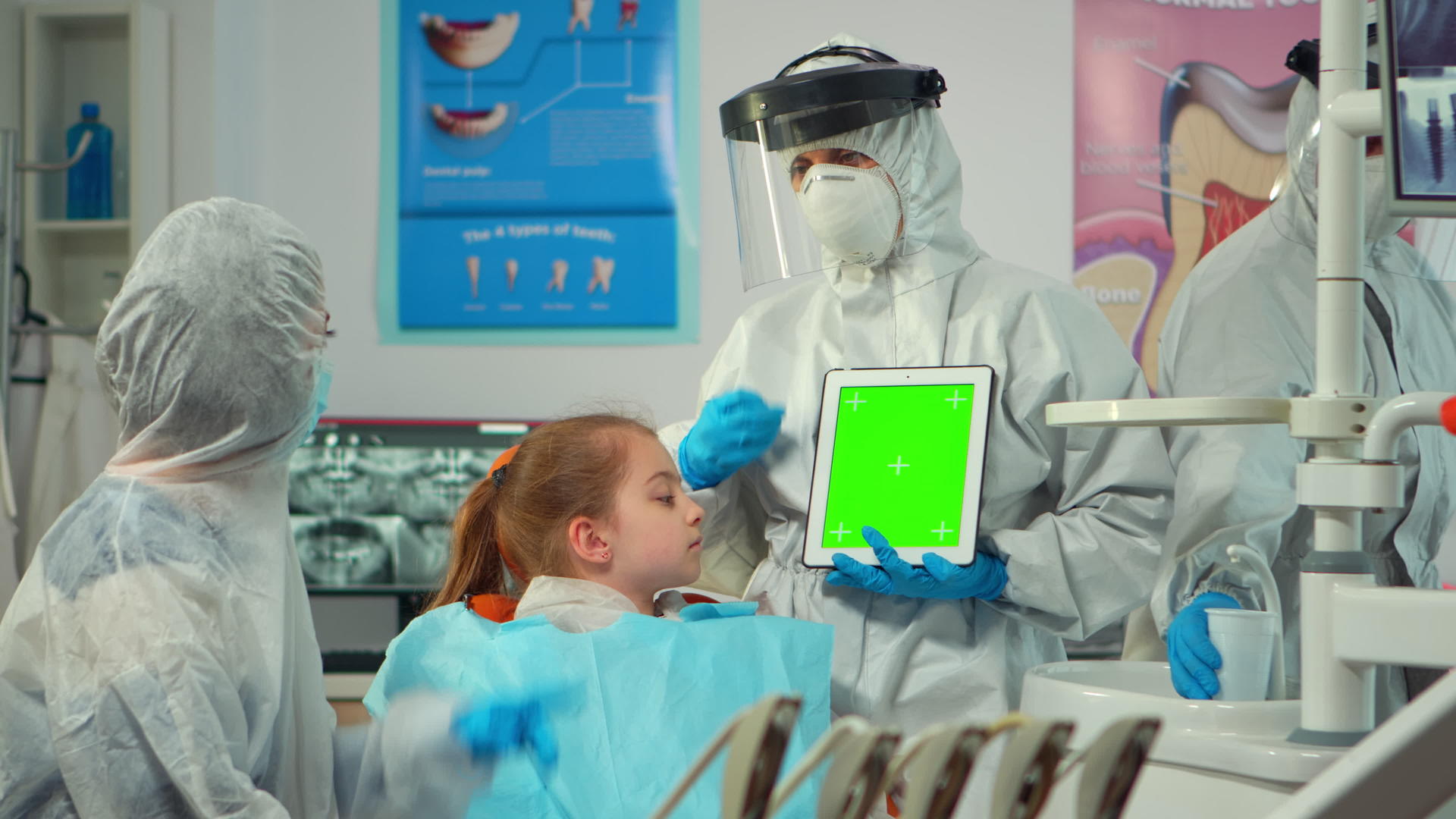 戴着面具的牙医指着绿屏显示器和孩子们交谈视频的预览图