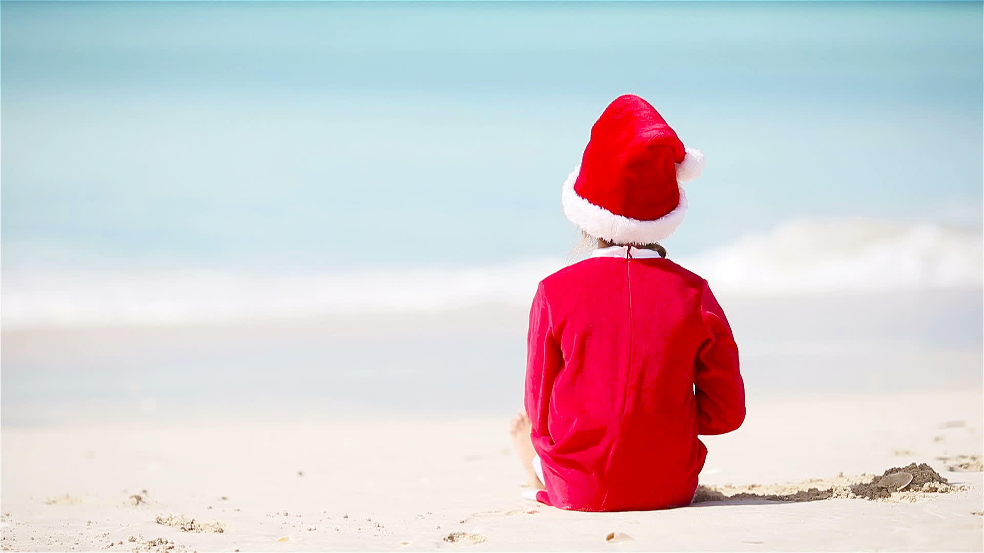 圣诞节期间在白色海滩上戴圣诞帽的小女孩视频的预览图
