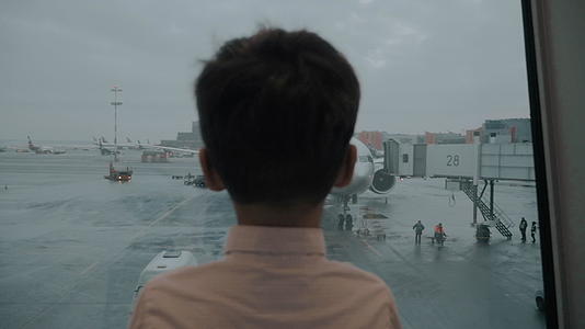 在等待飞行时男孩看着机窗中的飞机视频的预览图