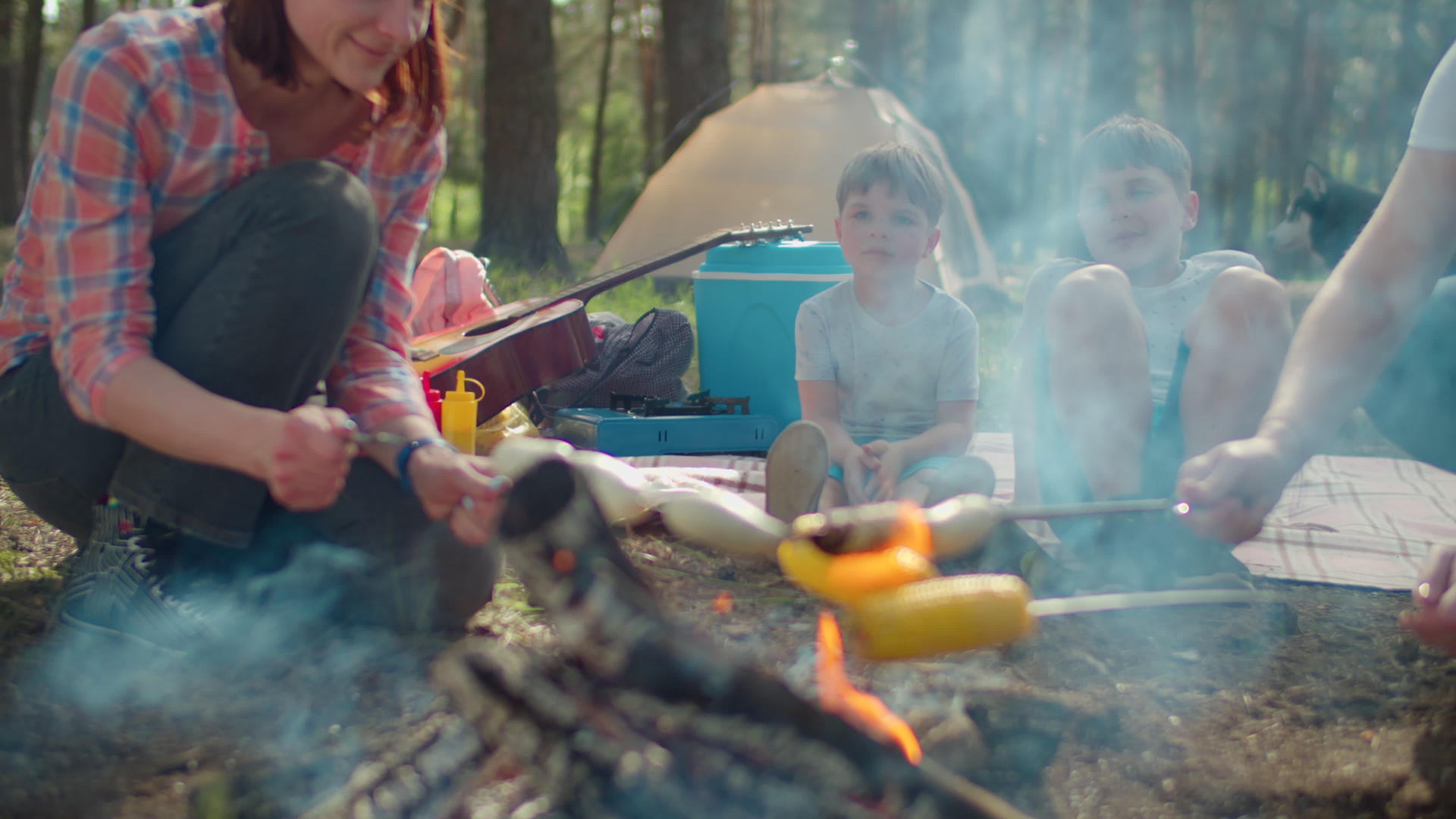 在夏天的家庭野营度假期间两位母亲在森林的帐篷里煮香肠视频的预览图