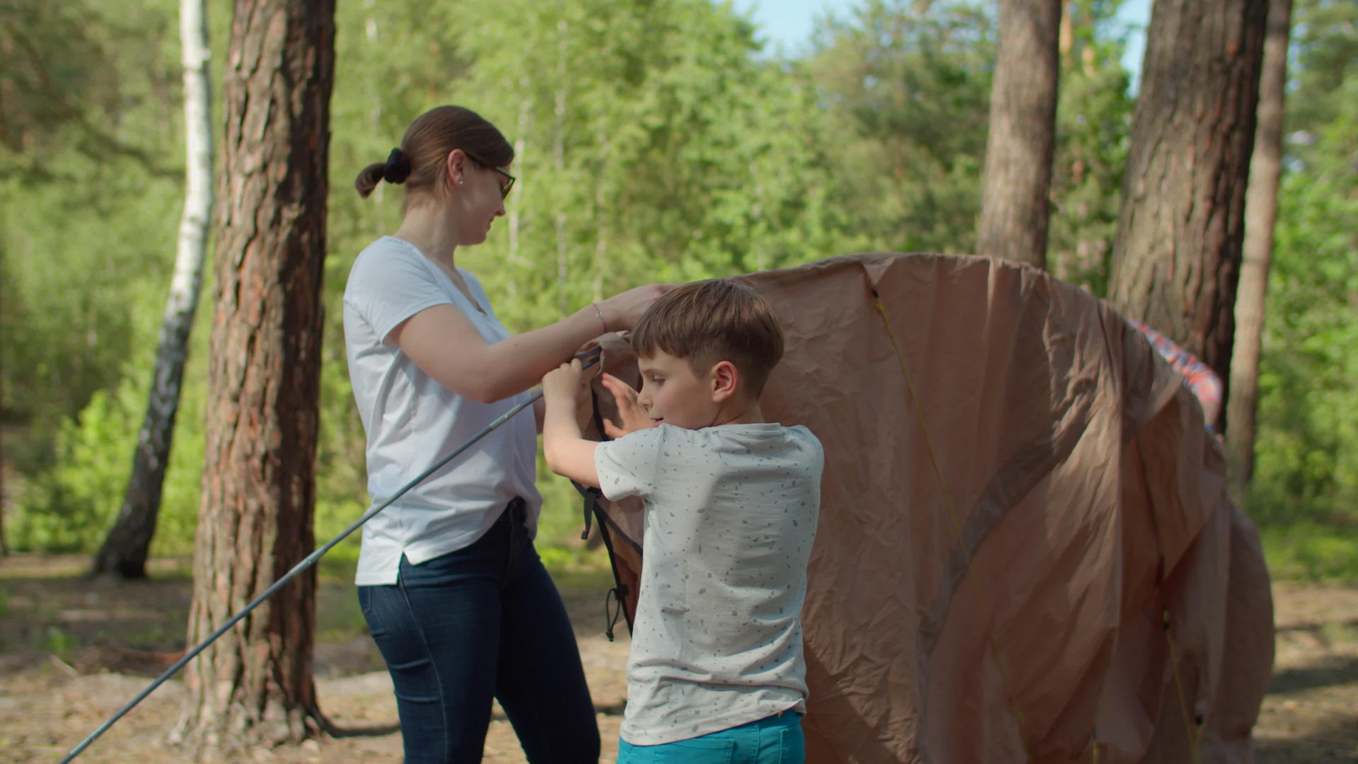 两个男孩帮助两个母亲在森林里搭起帐篷供当地家庭露营视频的预览图