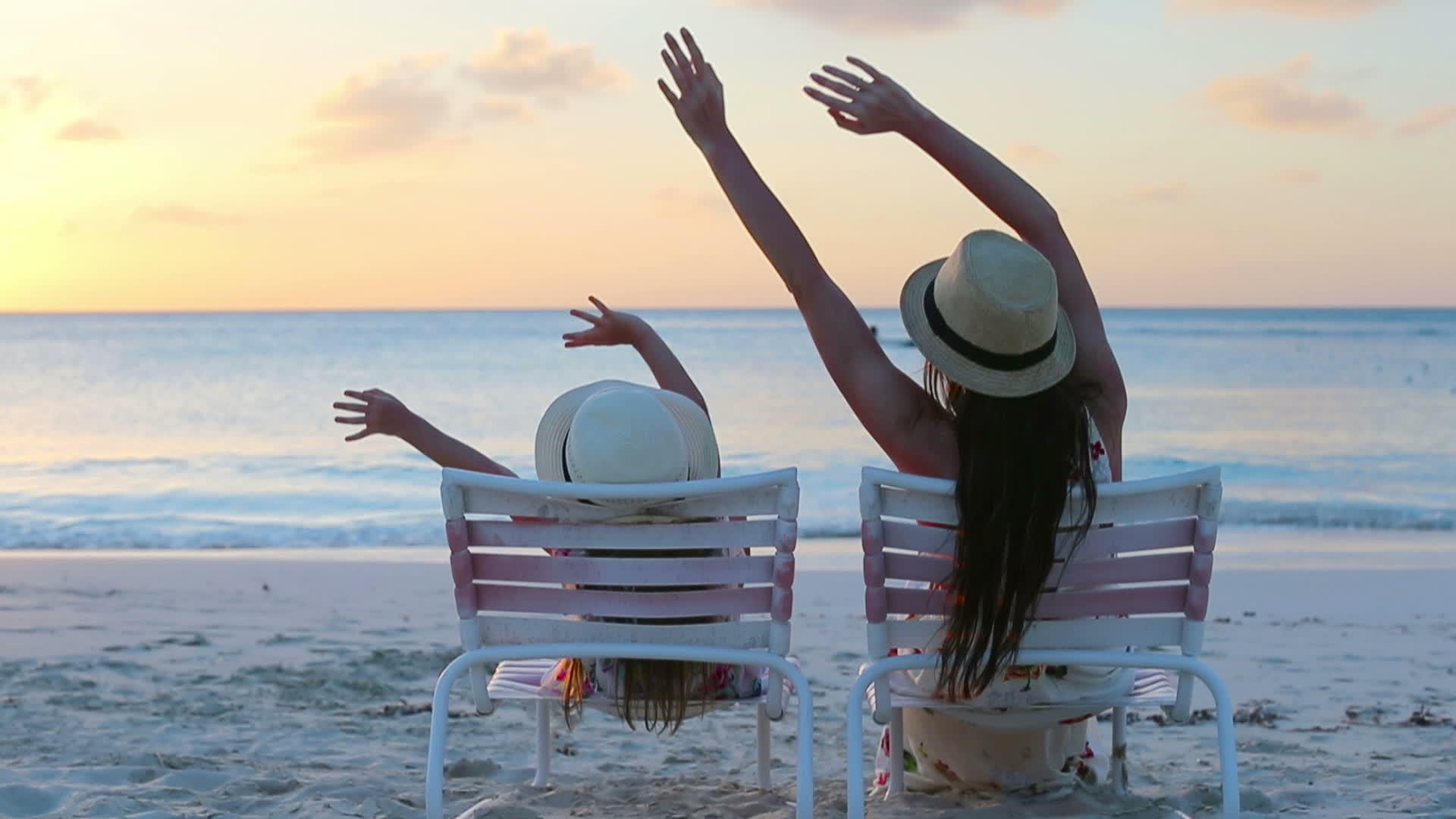 小女孩和妈妈在日落时坐在沙滩椅上视频的预览图