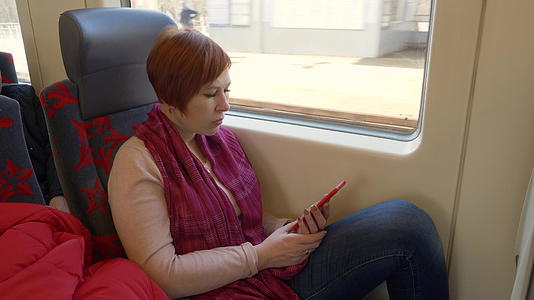 女旅行者坐在移动火车的窗口背景上看着智能手机视频的预览图