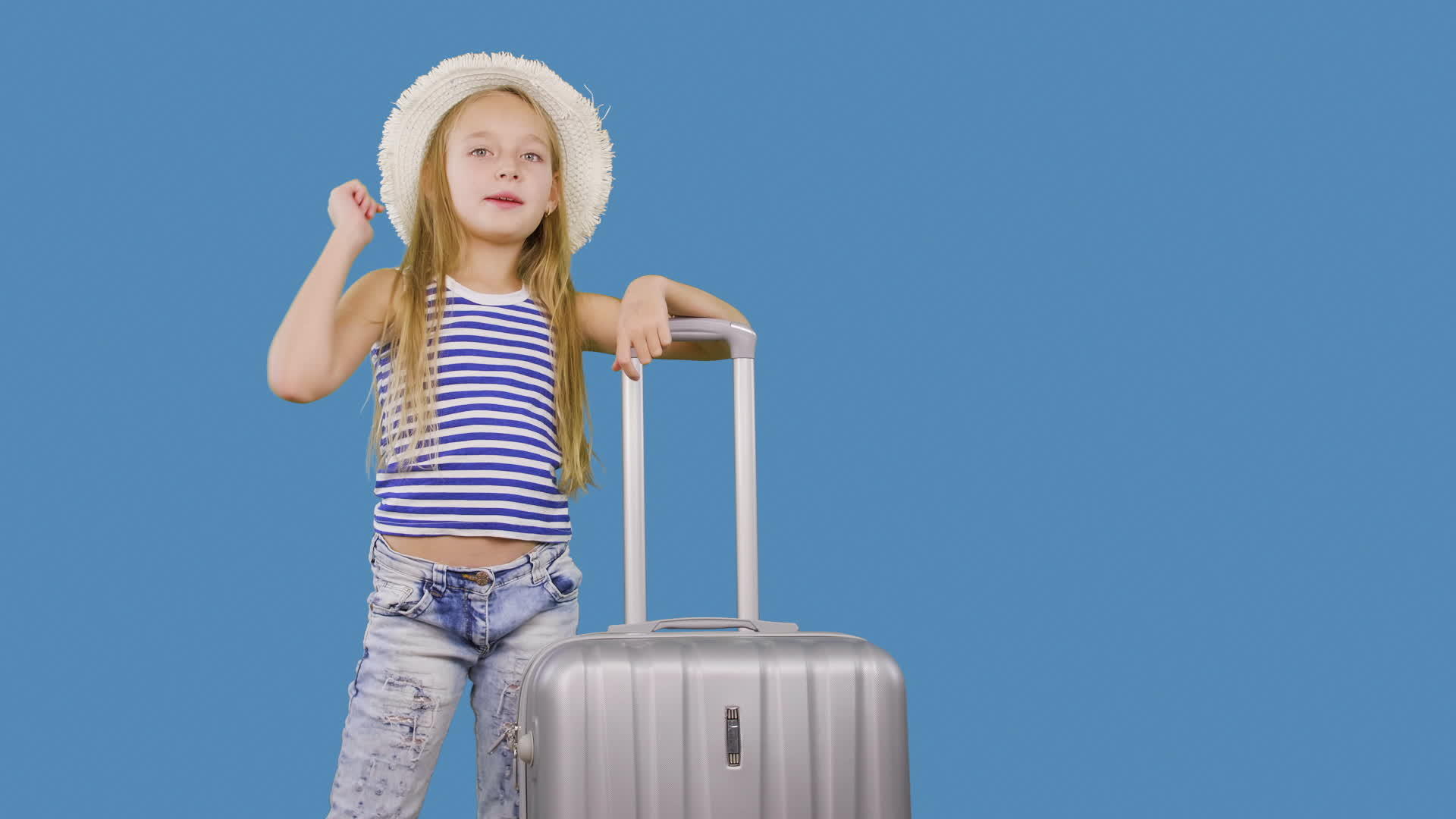 旅行中的女孩在工作室的蓝色背景上用手提箱打招呼视频的预览图
