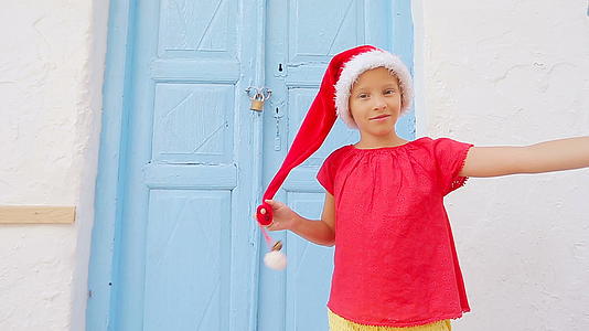 在米科诺斯岛的老街上戴着红色圣诞帽的小女孩在户外自拍视频的预览图
