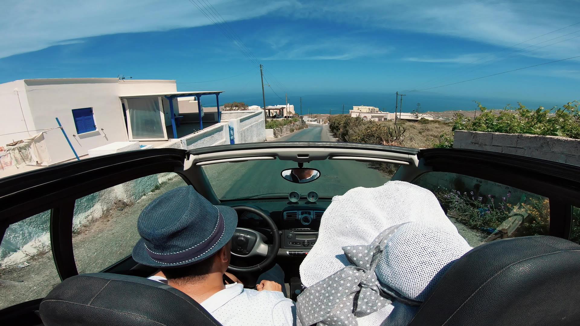 一对快乐的年轻夫妇在桑托里尼岛海岸驾驶敞篷车视频的预览图