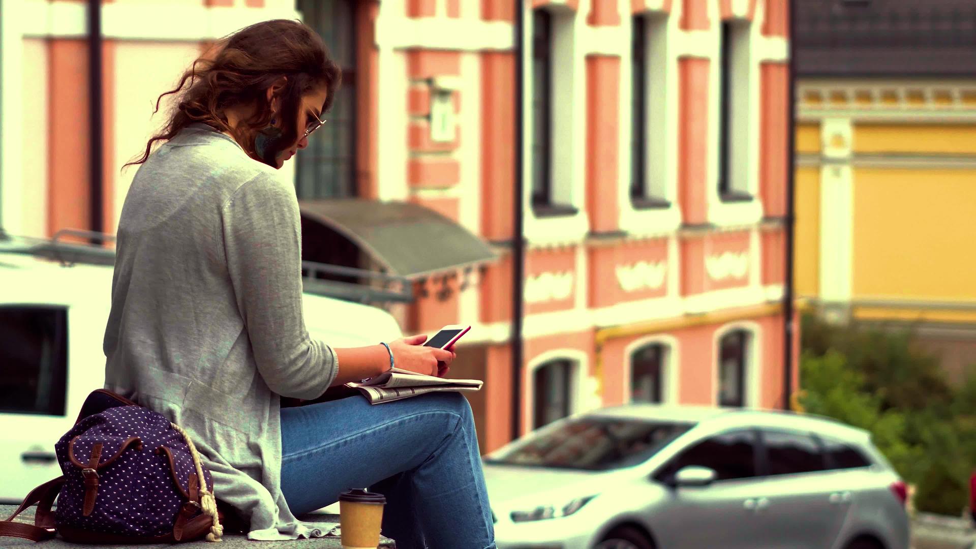 一段视频年轻的旅游妇女坐在市中心的栏杆上视频的预览图