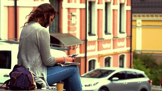 一段视频年轻的旅游妇女坐在市中心的栏杆上视频的预览图