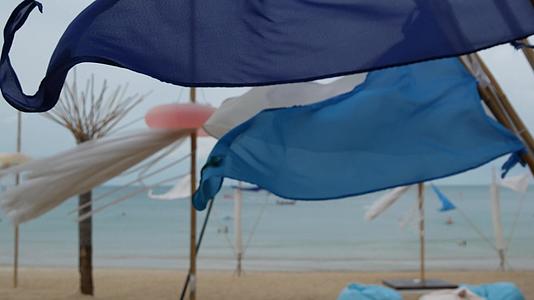 在热带海滩多云的天气里小三角蓝旗在风中飘扬视频的预览图