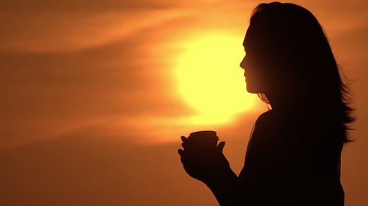 女人拿着杯子喝太阳在天空中升起视频的预览图