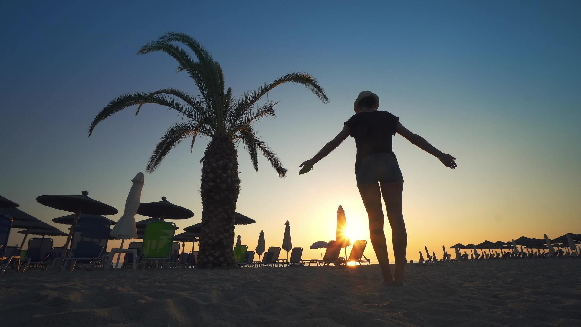 在海边的日出下有一个坚强自信的女人用棕榈树的圆影在海边张开视频的预览图