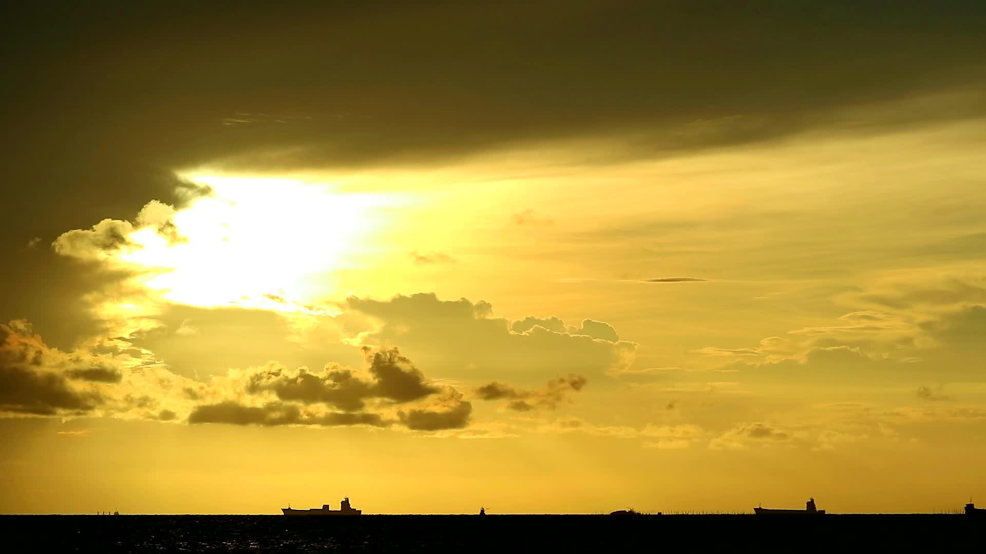 黄色、橙色的天空和深红色的云在海上移动和停泊在货船停泊的地方视频的预览图