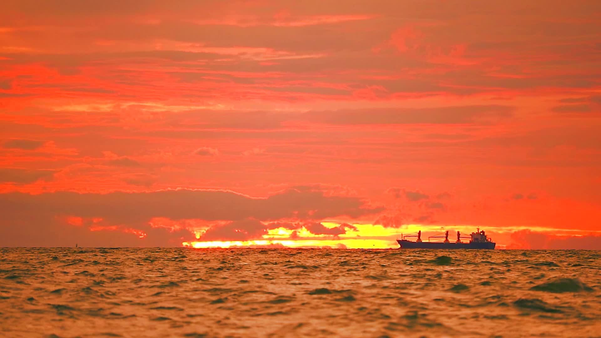 停泊在海面上的货船和日落天空中的红云视频的预览图
