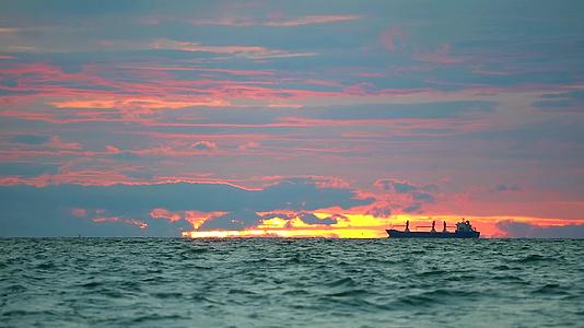 停泊在海面上的货船和日落天空中的暗红云视频的预览图