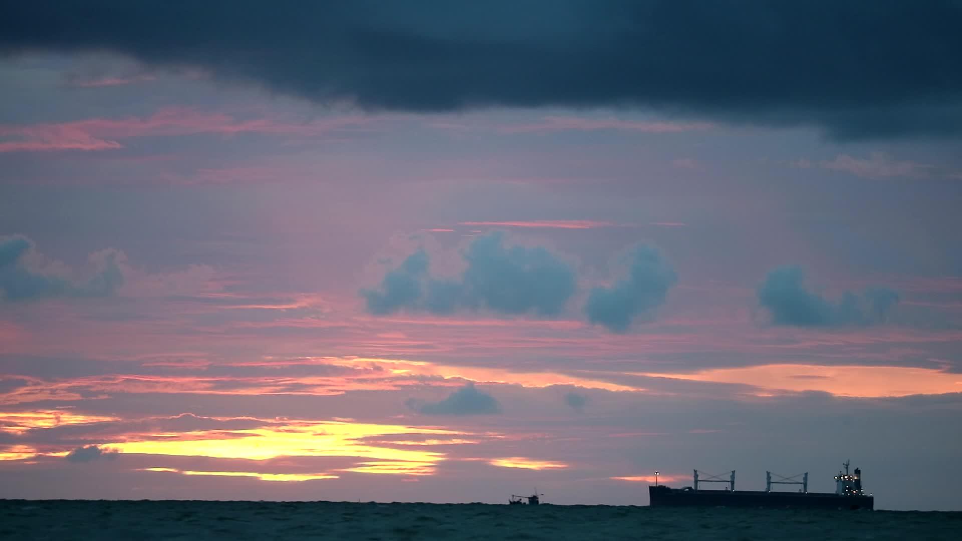 日落、天空和黑暗的红云漂浮在海上的光船和渔船上视频的预览图