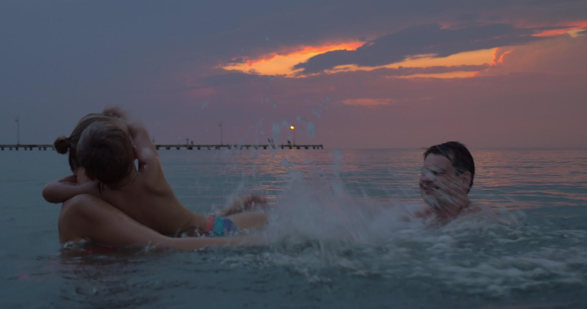 日落时母亲和儿子在城市的海里游泳视频的预览图