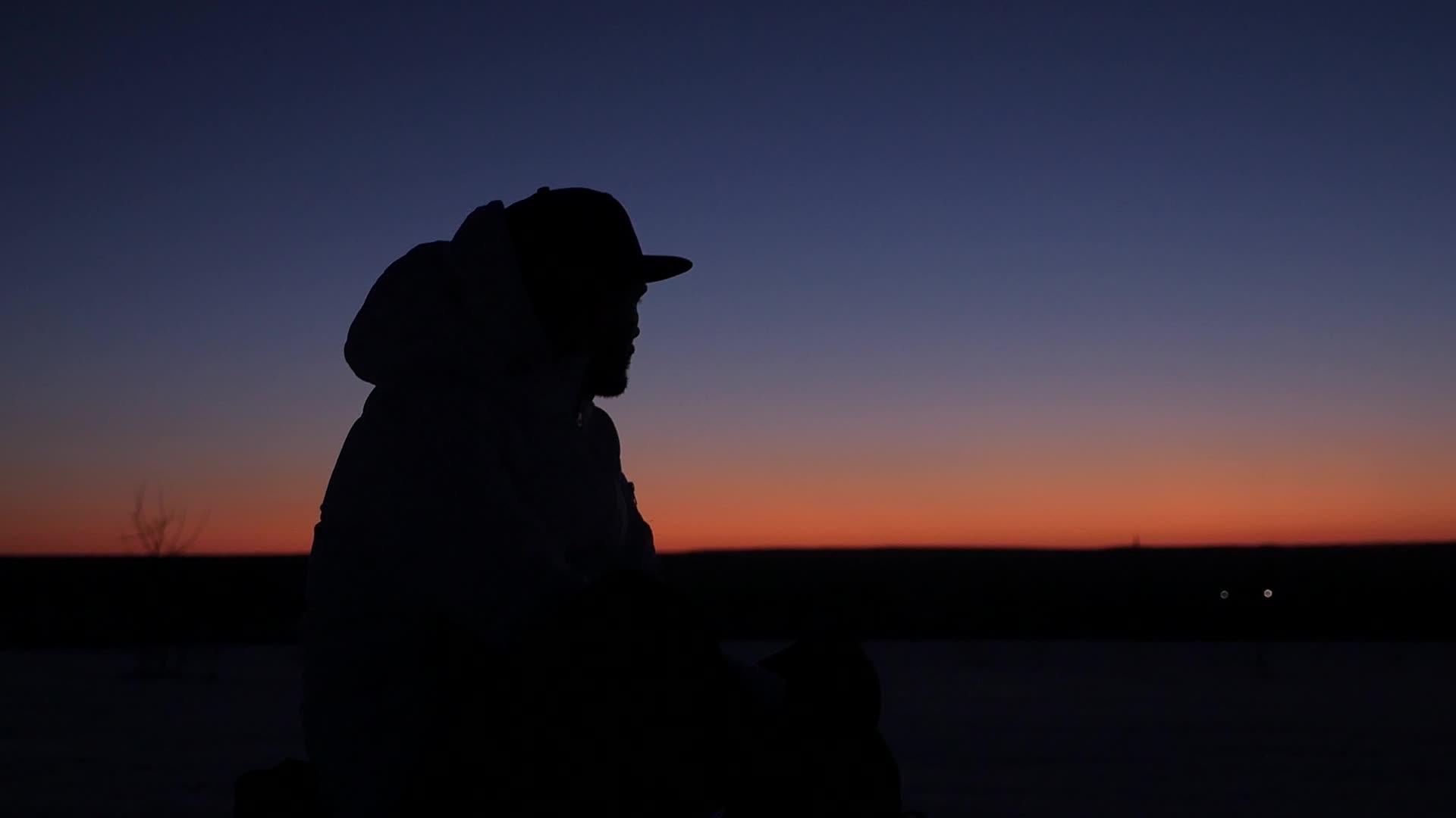 一个戴着帽子的年轻人在日落和梦想中安心地坐着视频的预览图