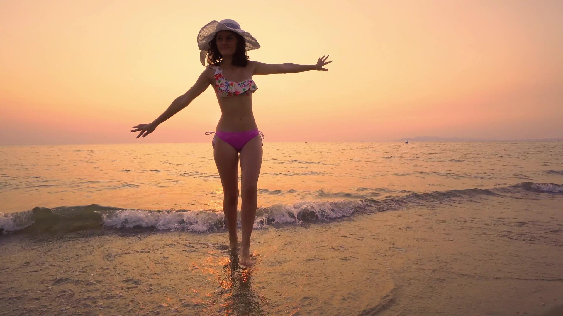 戴着帽子享受美丽的日落走出海滩的水面视频的预览图