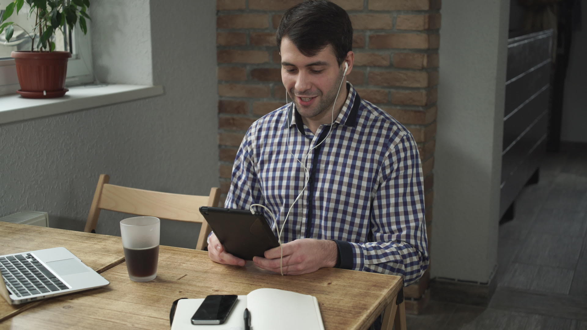 一名男子坐在桌子上用平板电脑耳机在耳朵里聊天视频的预览图
