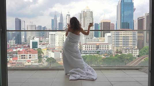 穿着白色毯子的女孩在阳台上快乐地跳舞俯瞰现代城市视频的预览图