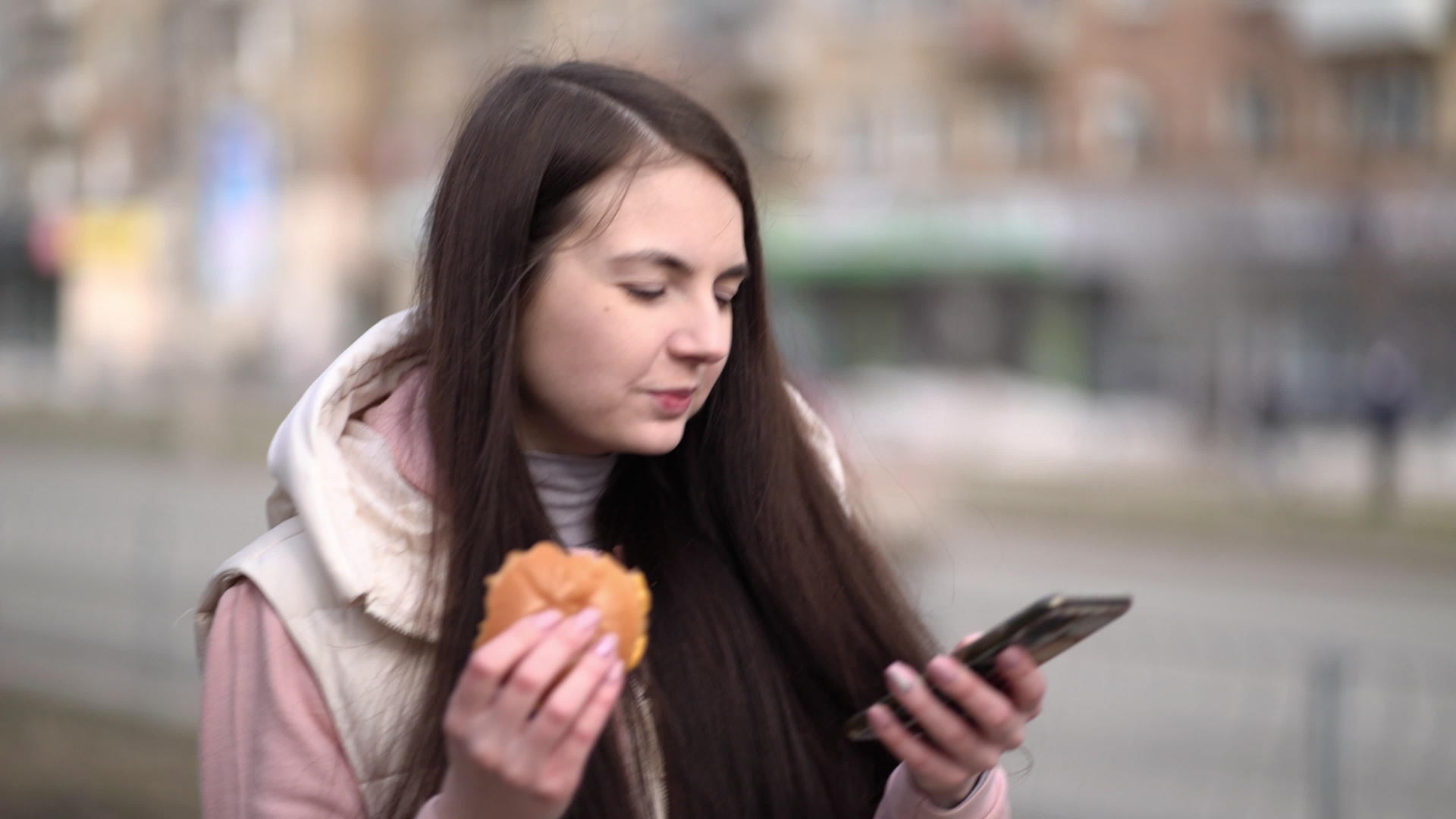 享受汉堡快乐的女人拿着智能手机在城市户外散步视频的预览图