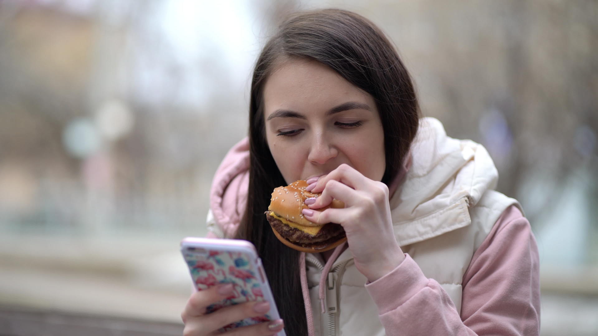 快乐的女人在街上用智能手机吃汉堡视频的预览图