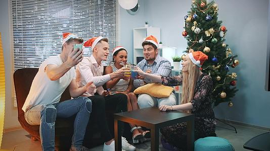 快乐的朋友在圣塔帽在圣诞派对上通过智能手机播放视频视频的预览图