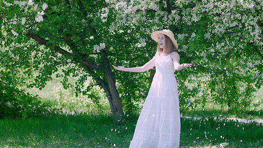 快乐的年轻女孩在夏天的果园里享受着落下的苹果树花瓣视频的预览图