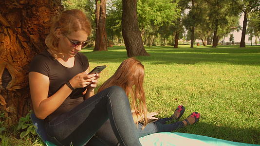母亲和女儿在公园里使用小工具视频的预览图