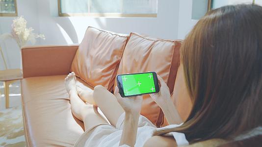 4K女性沙发上划手机播放绿幕素材视频的预览图