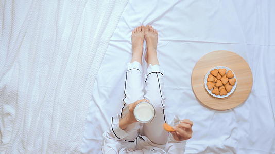 穿着白睡衣的女人喝牛奶吃饼干坐在床上视频的预览图