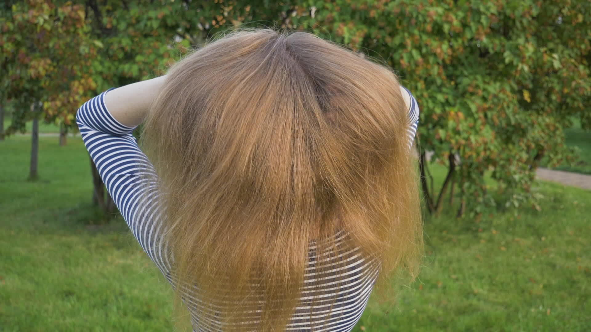 在绿色公园里年轻的金发女郎用手扔掉了健康的长发视频的预览图