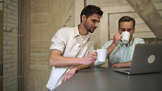 两个年轻的职业男人喝咖啡找电脑聊天视频的预览图
