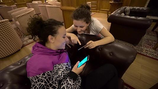 不同的女孩朋友在沙发上微笑着看着智能手机照片视频的预览图