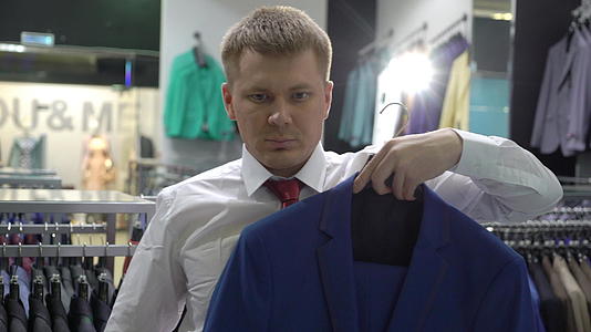购物和时尚概念青年男子在商场选择和试穿夹克视频的预览图