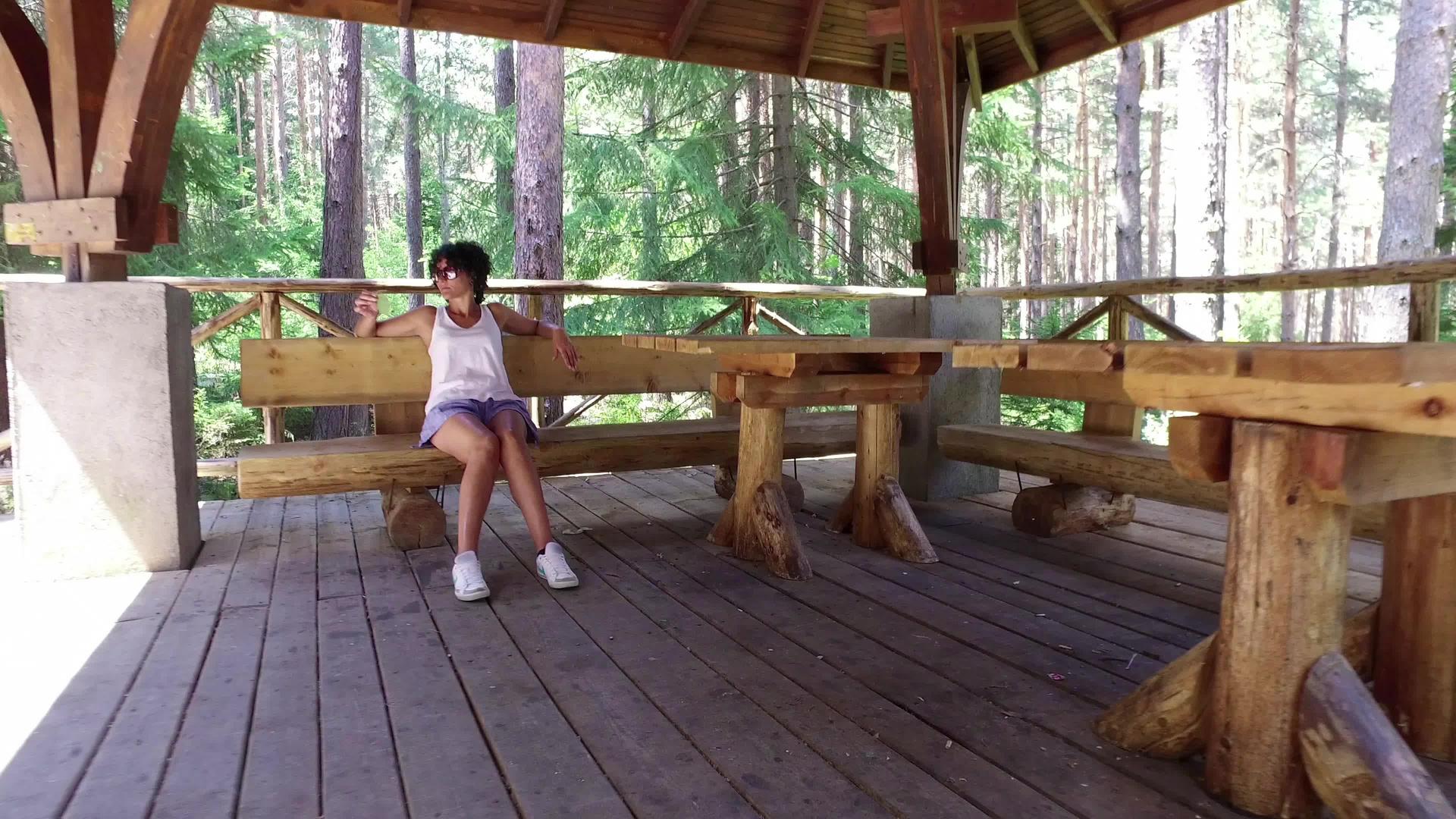 快乐的年轻女子坐在阳台的长凳上在农村松林的木屋里视频的预览图