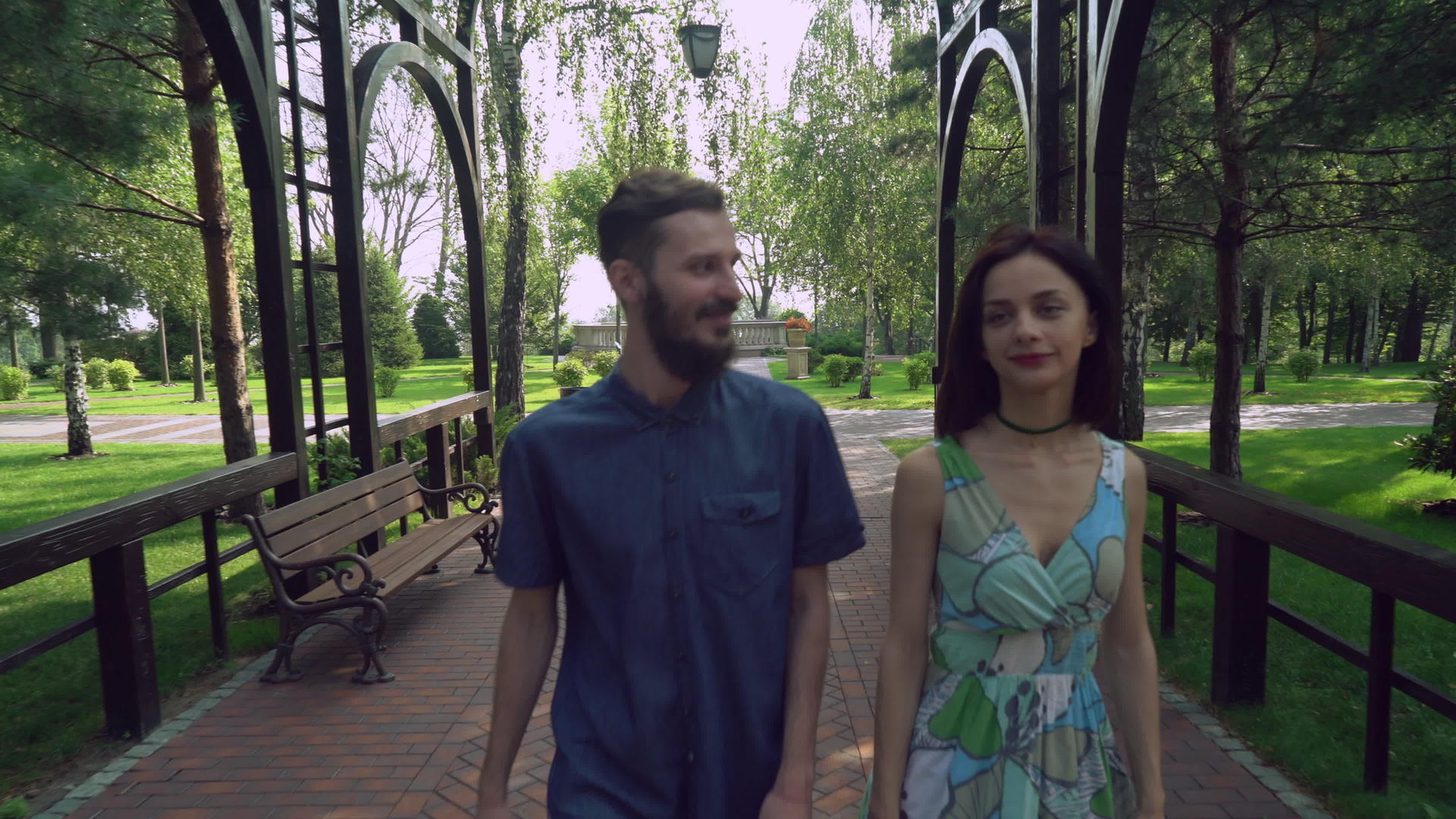 年轻夫妇走在公园的一条小路上在拱门下聊天和微笑视频的预览图